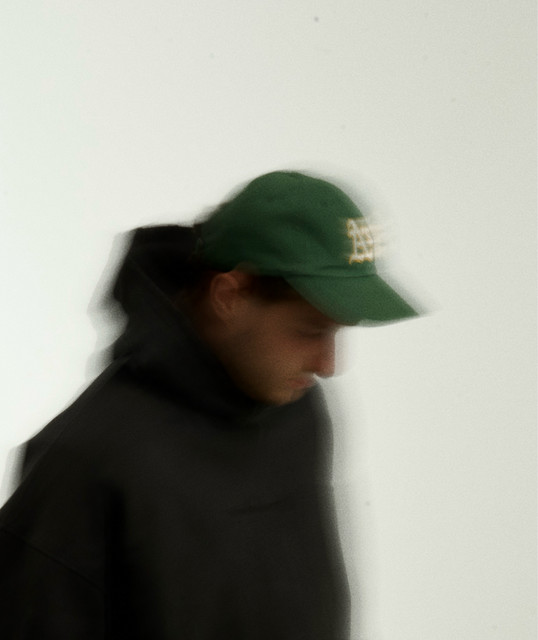 Paccu wearing a green cap and dark jacket in a softly blurred portrait.